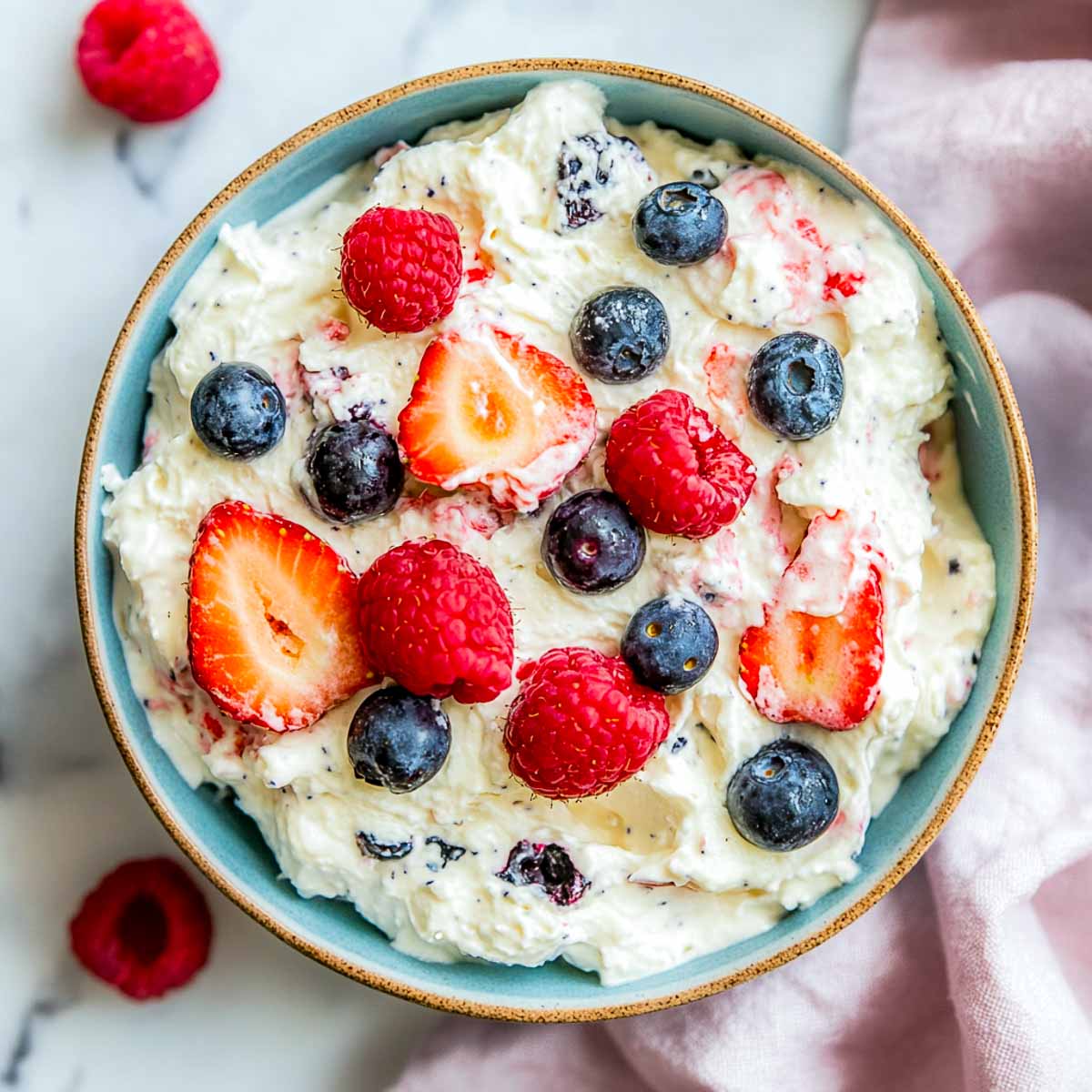 Creamy cheesecake berry salad with strawberries, raspberries, and blueberries in pastel blue bowl.