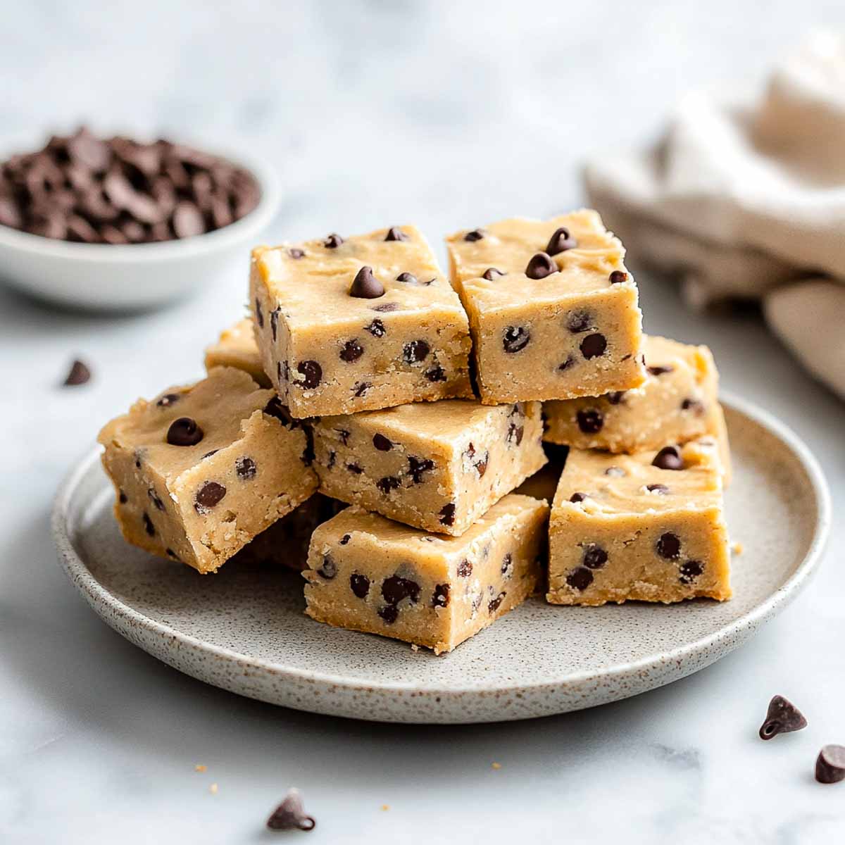 Stack of thick no-bake cookie dough bars with mini chocolate chips on a cream plate.