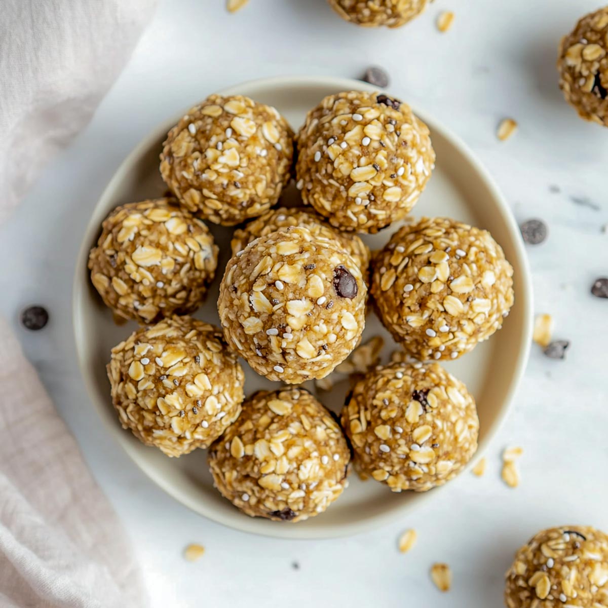 Golden oat and chia energy balls stacked on cream plate with scattered oats.
