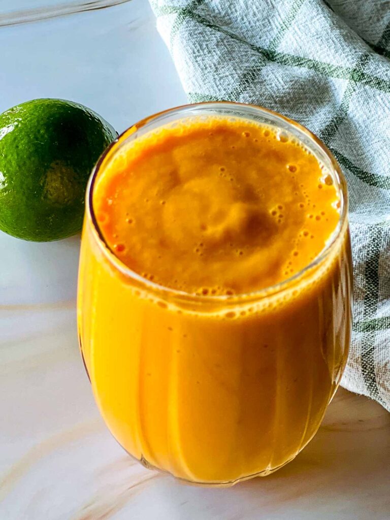 A glass of papaya smoothie placed on a marble surface.