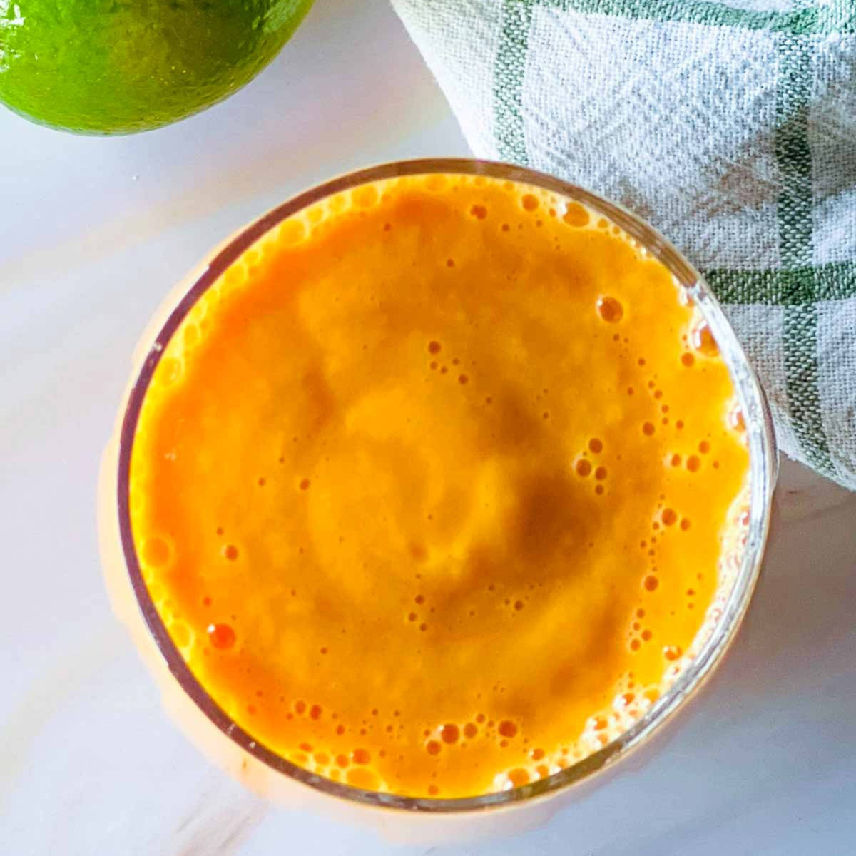 Top view of a glass of papaya smoothie placed on a marble surface.
