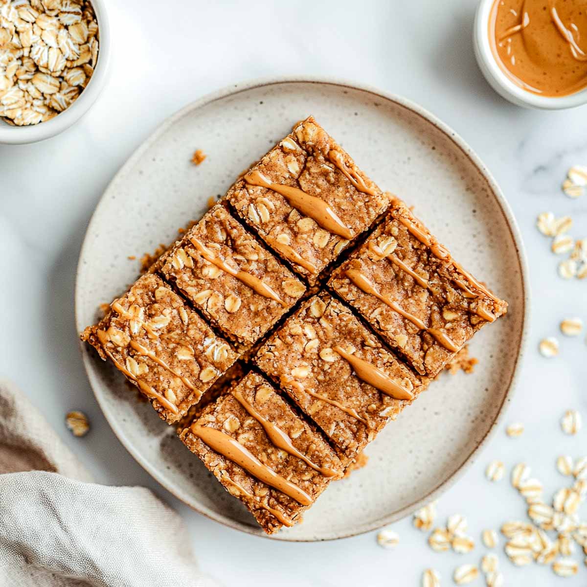 Rustic peanut butter oat bars with oat flakes and light peanut butter drizzle on cream plate.
