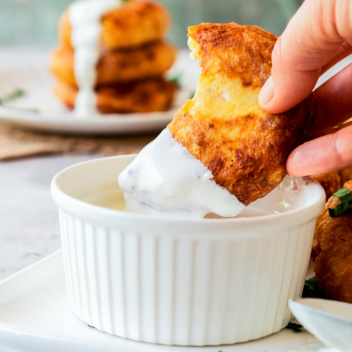 A bitten potato fritter dipped into white dipping sauce.