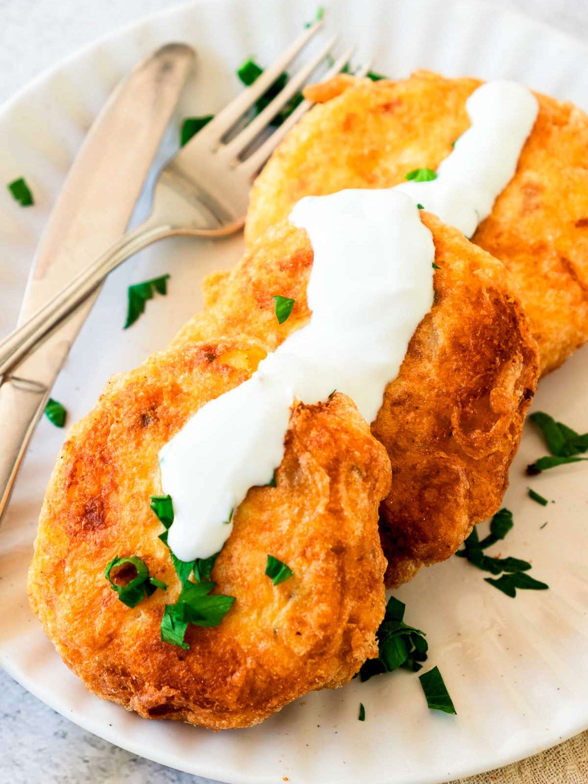 Three potato fritters on a small serving plate drizzled with white dip.