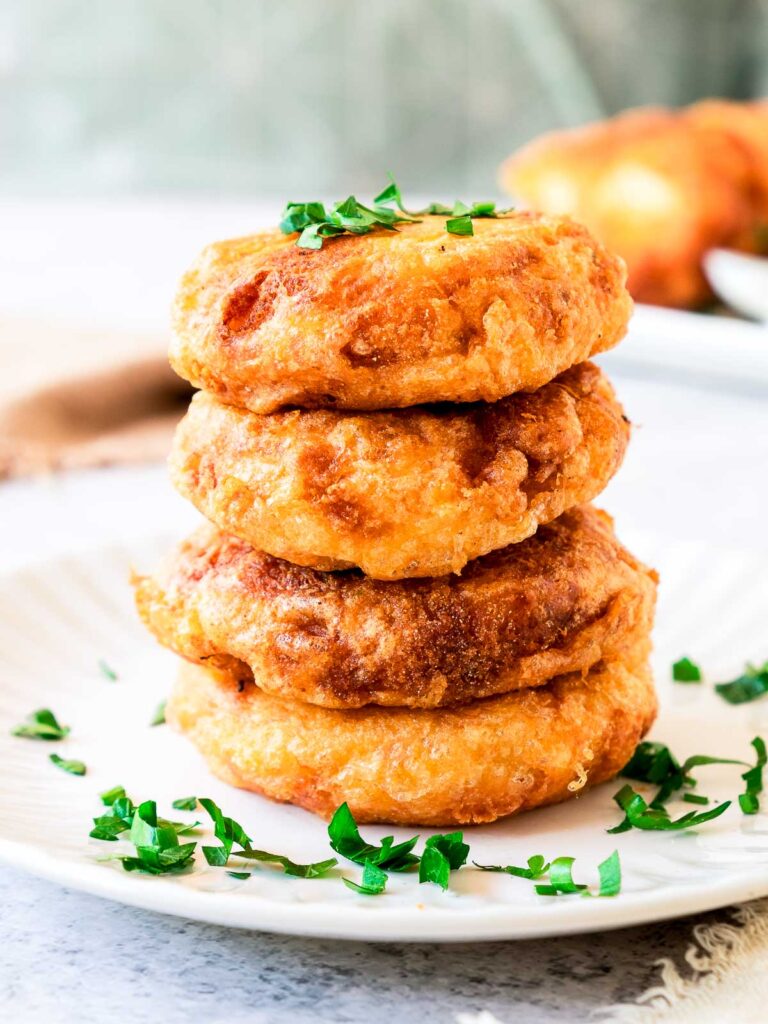 A stack of potato fritters on a white serving plate.