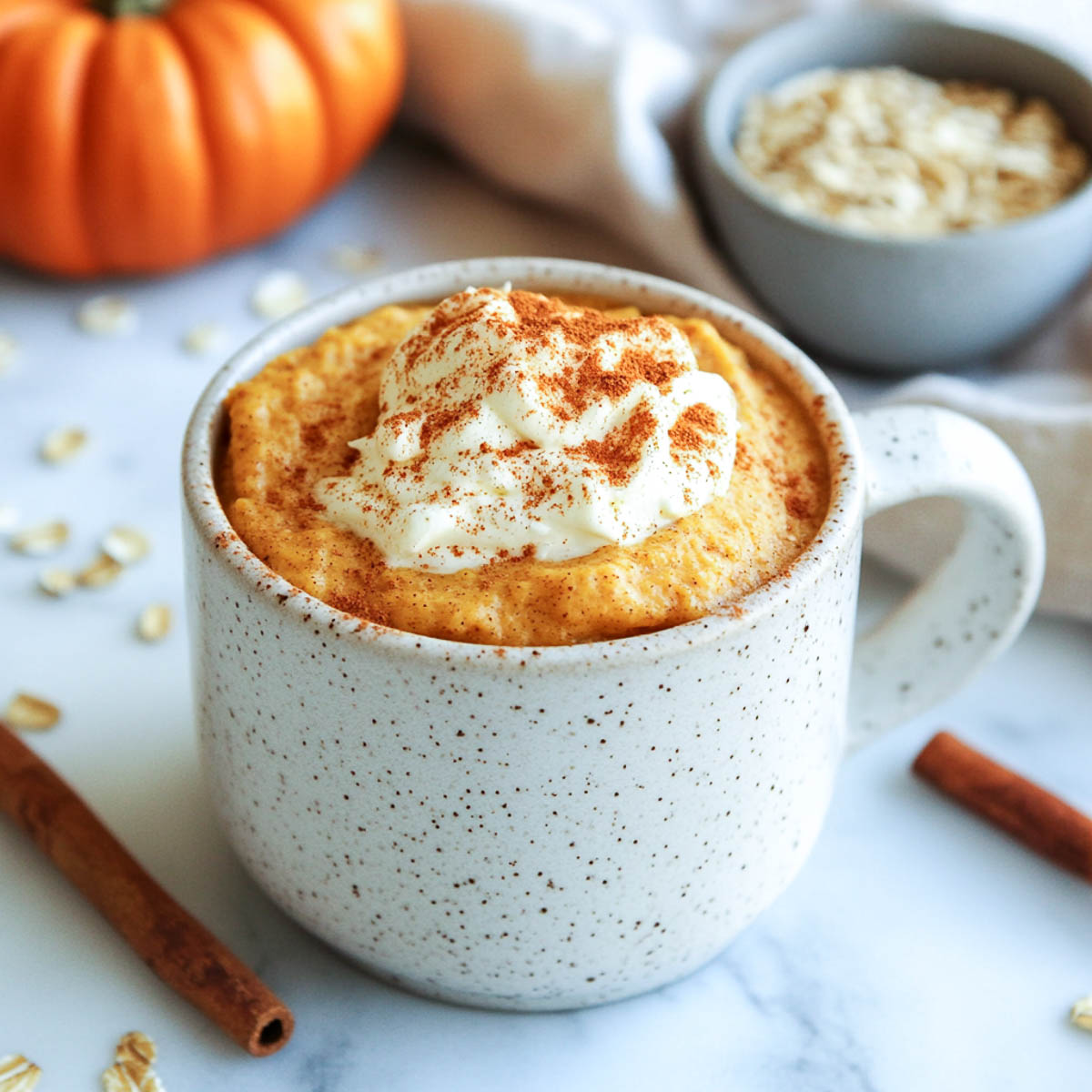 Pumpkin spice protein mug cake with whipped topping in a speckled mug.