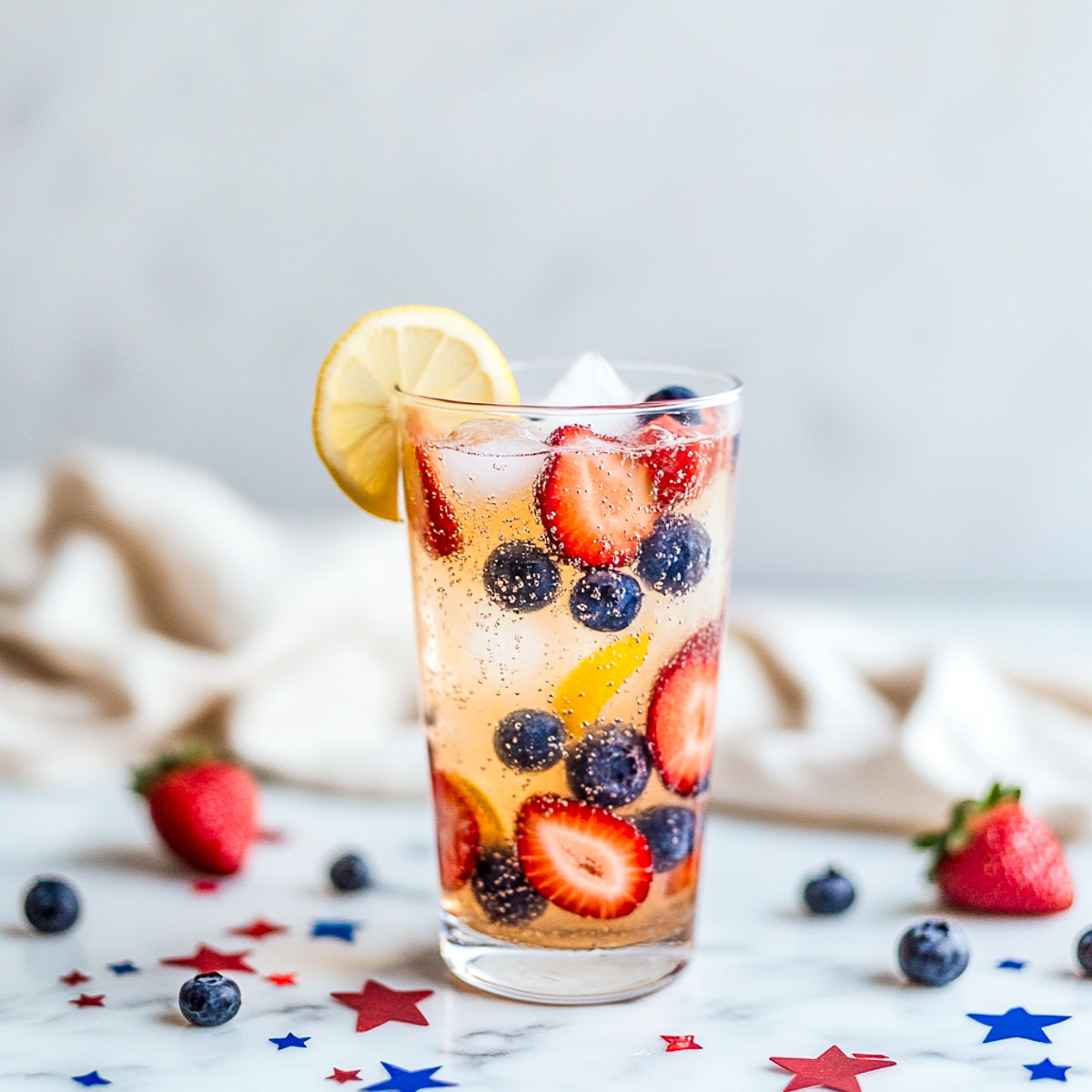 Tall glass of sparkling fruit mocktail with strawberries, blueberries, and lemon.