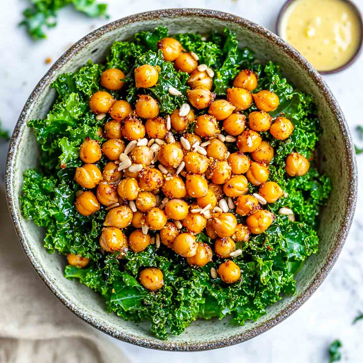 Rustic bowl of kale salad topped with roasted chickpeas and sunflower seeds.