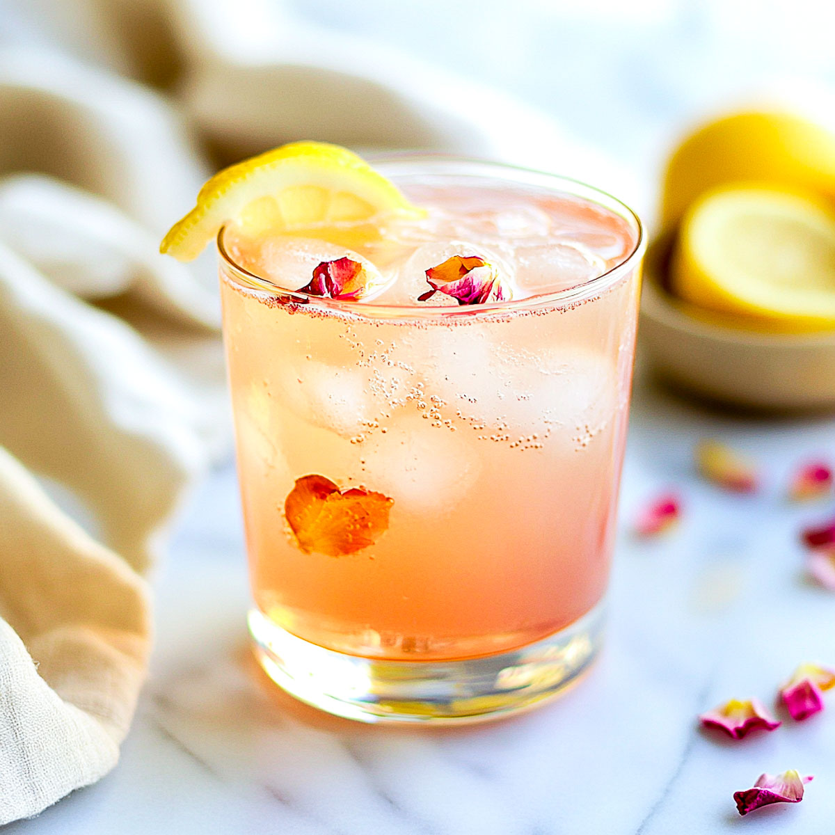 Rose lemonade mocktail with lemon twist and rose petals in a clear glass.