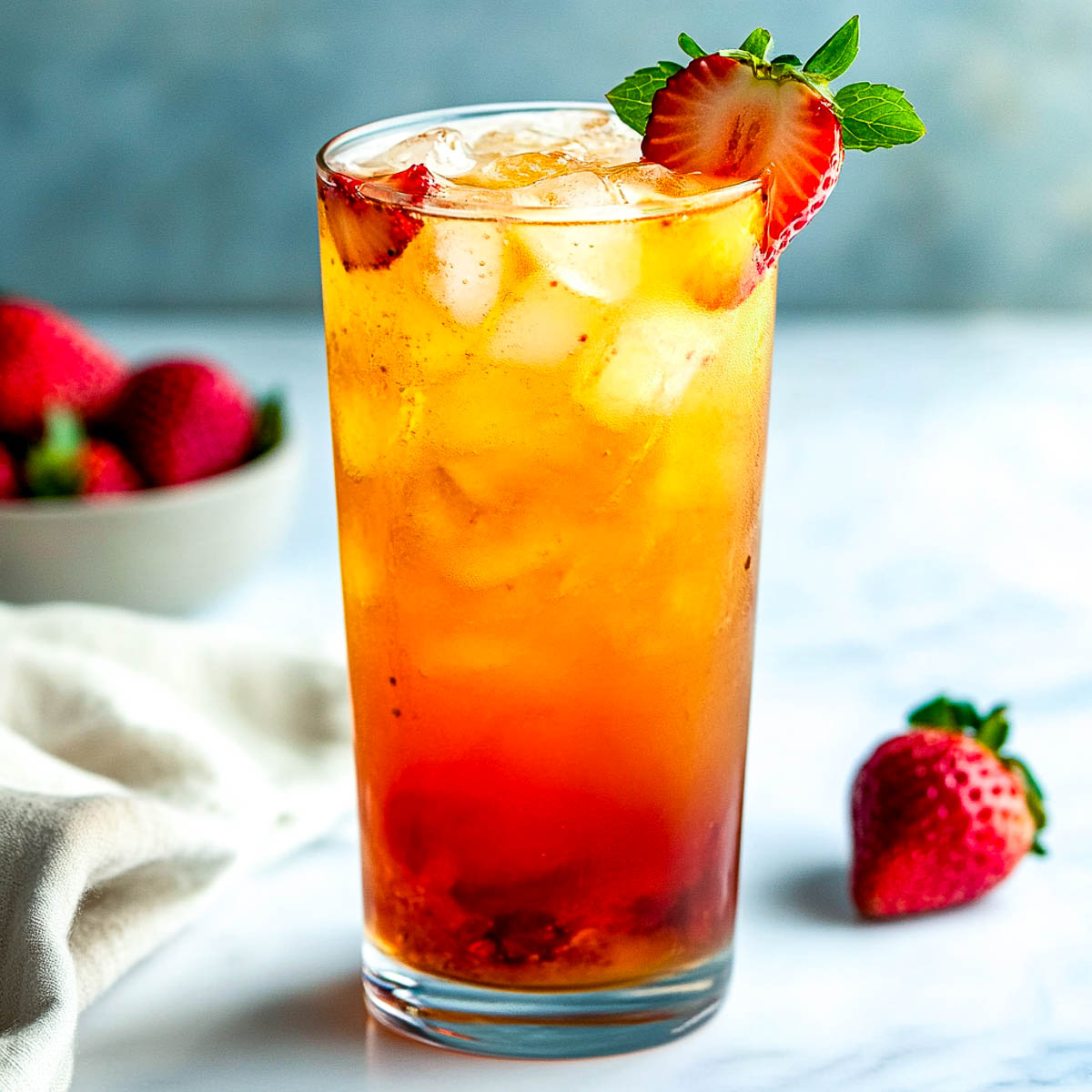 Sparkling strawberry sweet tea with muddled fruit, ice, and mint garnish.