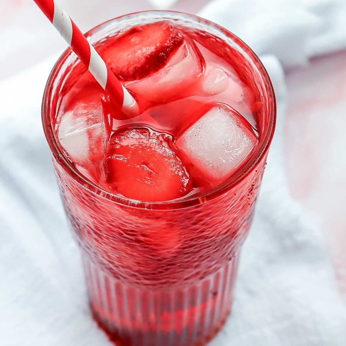 Strawberry acai refresher in a tall glass topped with ice cubes.