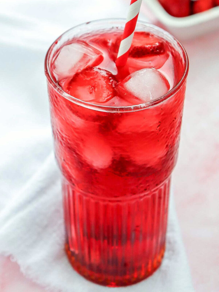 Strawberry acai refresher in a tall glass placed over a pink surface.
