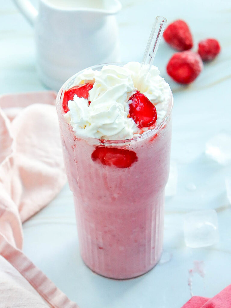 A tall glass of strawberry cheesecake frapuccino topped with whipped cream.
