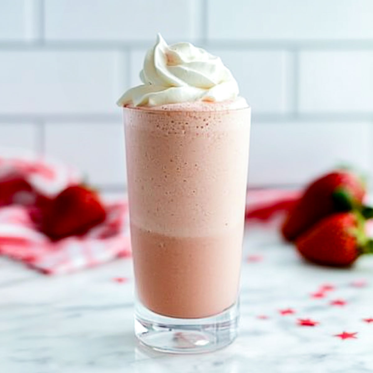 Tall glass of strawberry coconut mocktail with whipped coconut cream topping.