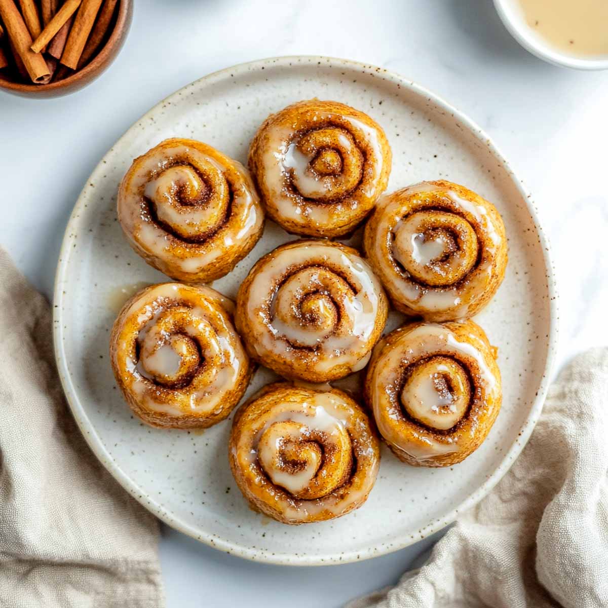 Golden sugar-free cinnamon rolls with a light glaze swirl on ivory plate.