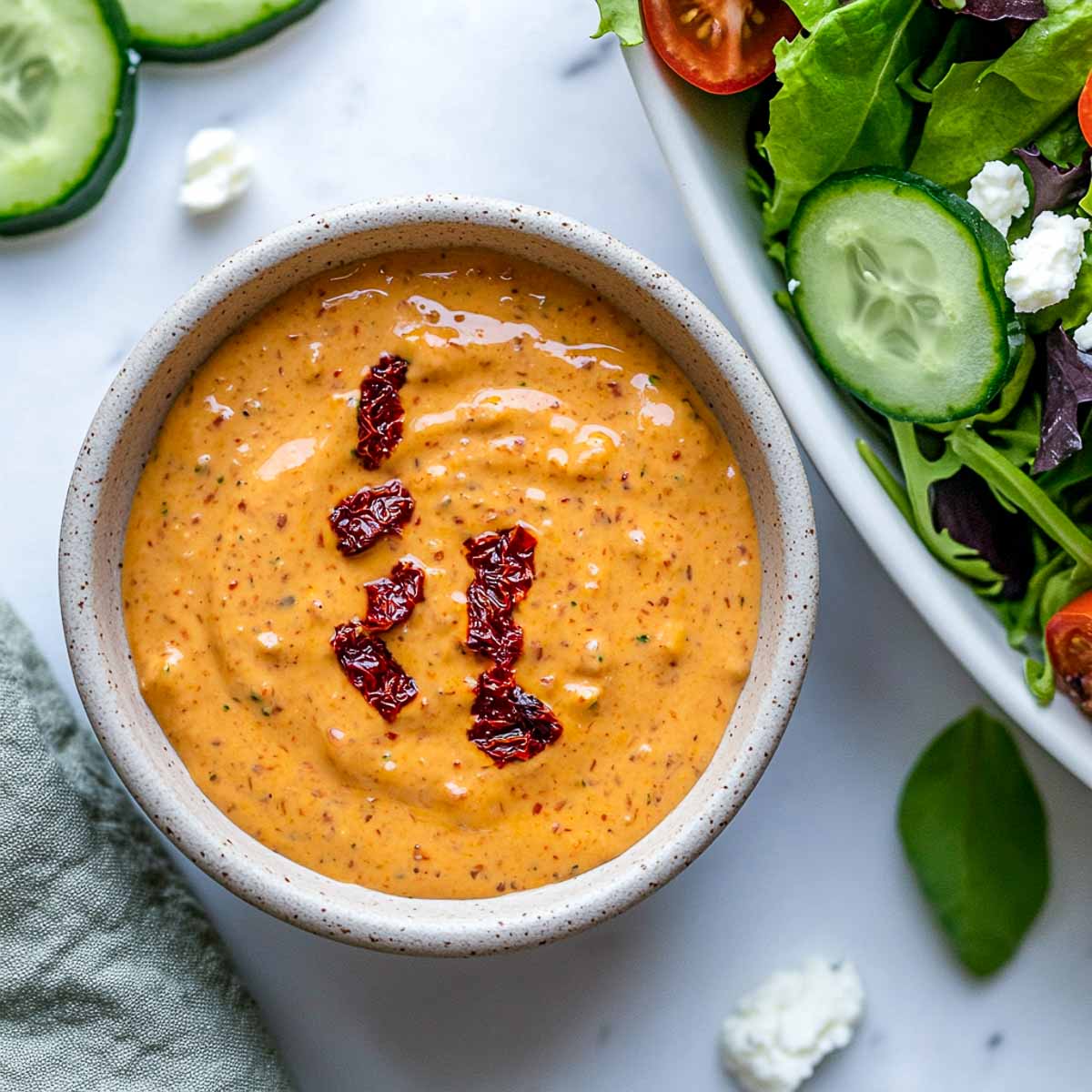 Sun-dried tomato Greek yogurt dressing with Mediterranean salad and cucumber slices.