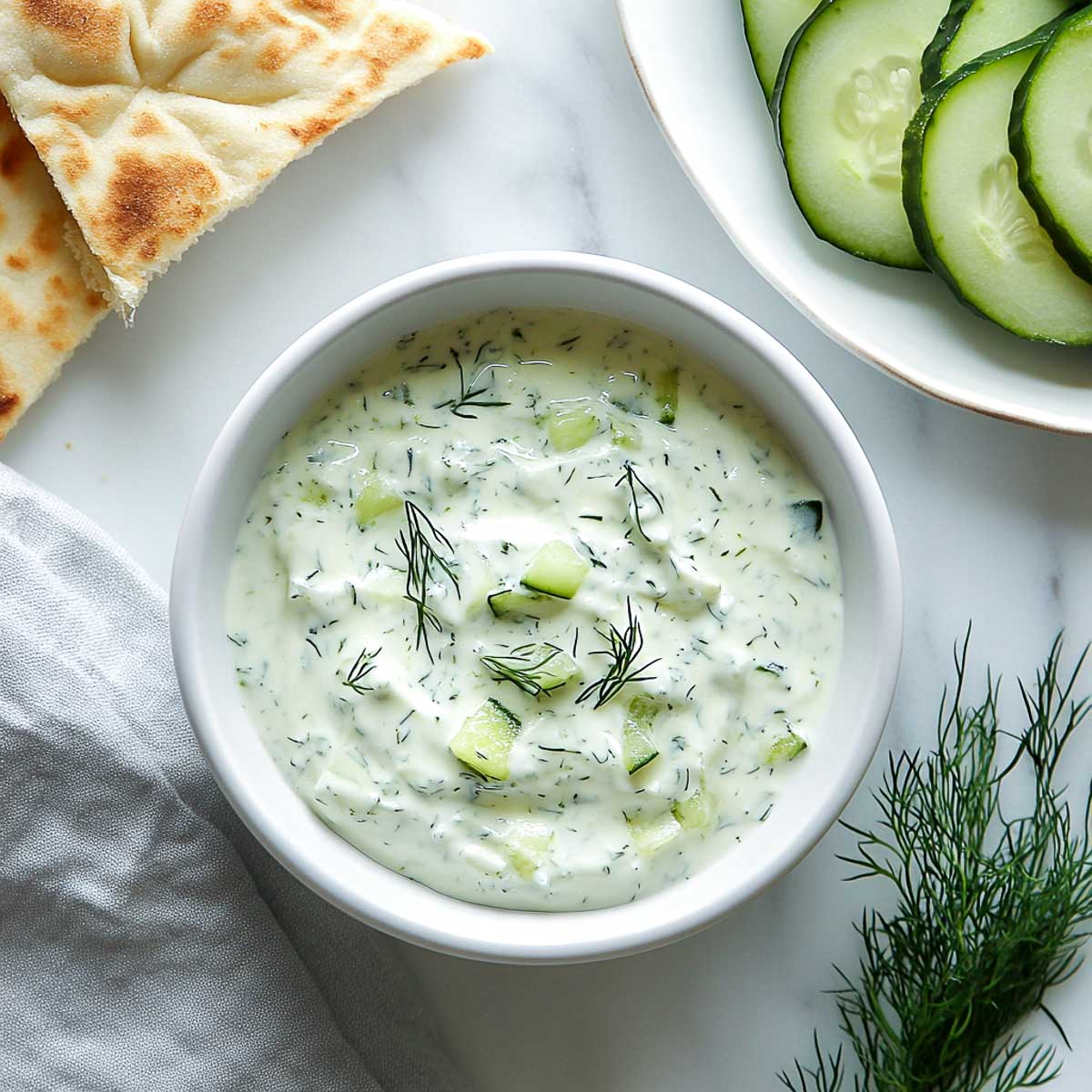 Tzatziki Greek yogurt dip with pita bread, cucumber slices, and fresh dill.