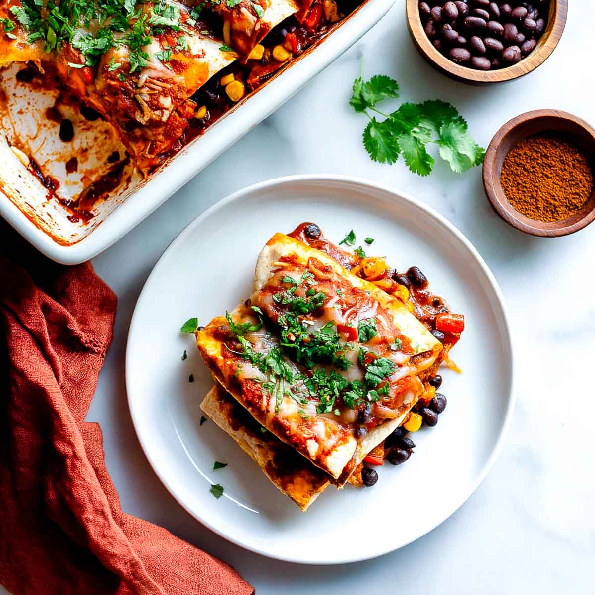 Vegan enchilada casserole served on a plate with black beans, corn, and cilantro.