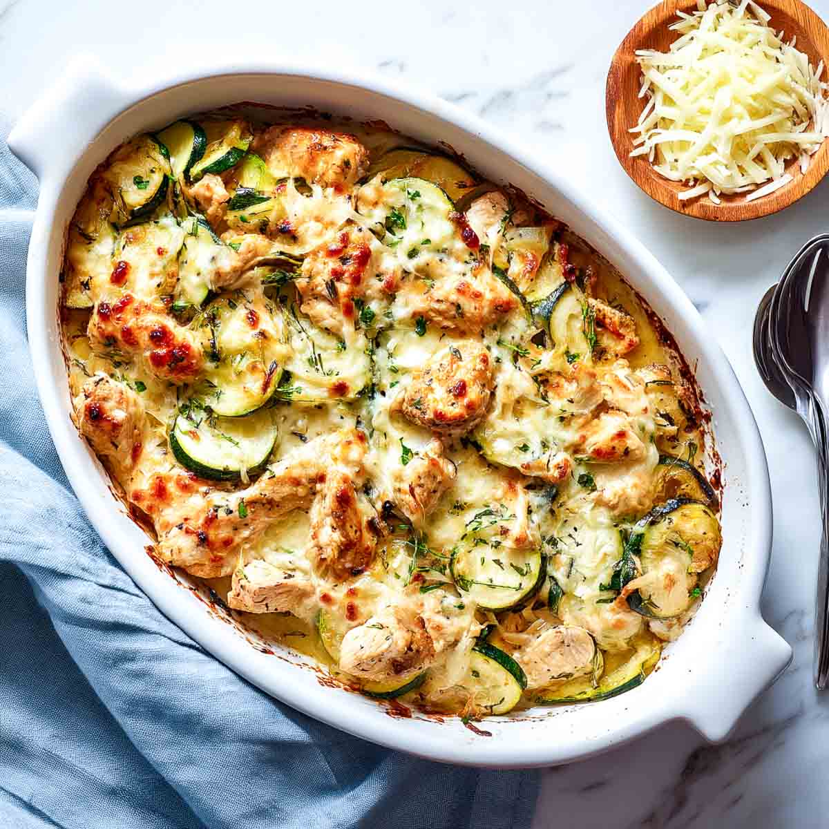 Cheesy chicken and zucchini bake with golden melted top in white dish.