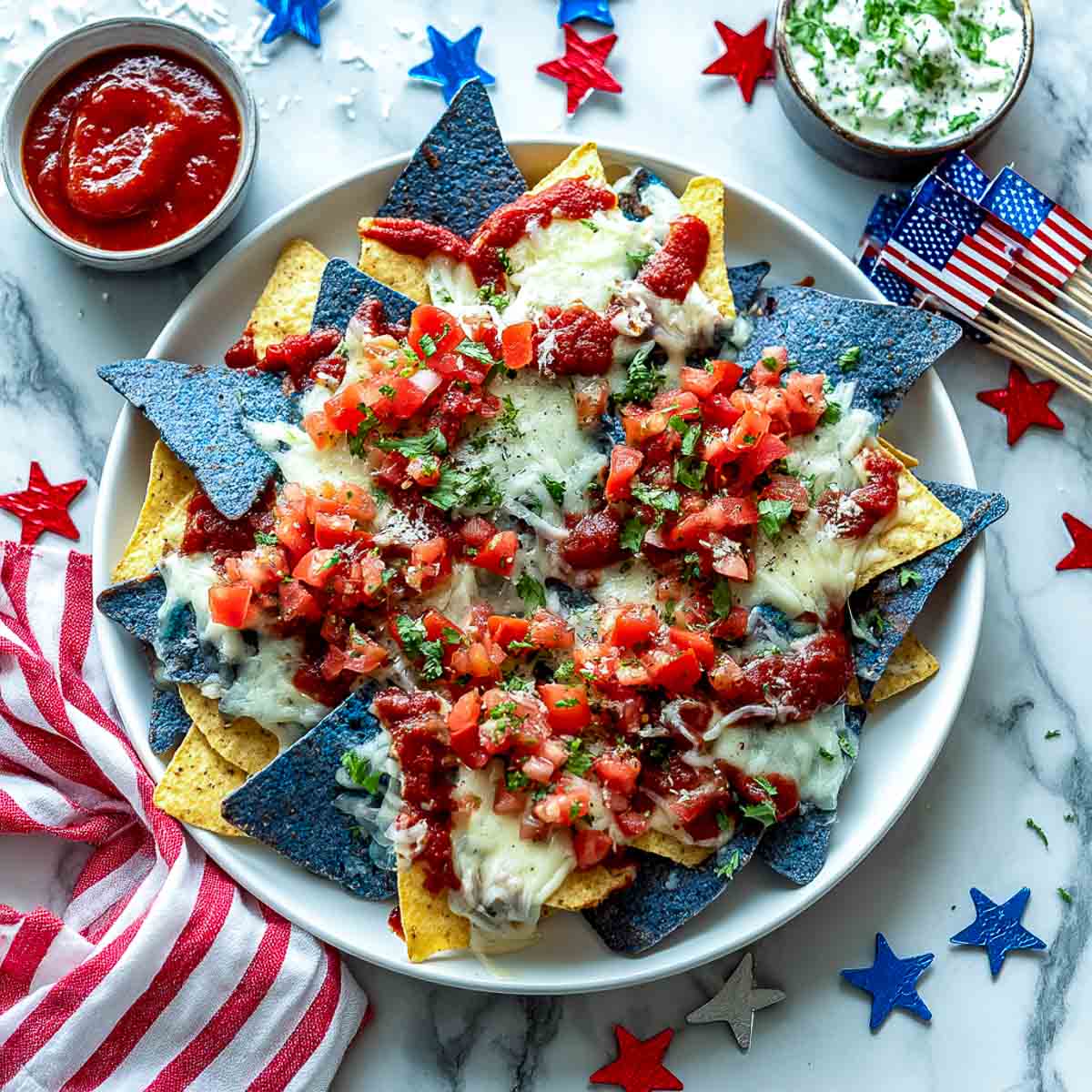 Nachos made with blue and yellow chips, melted cheese, salsa, and cilantro on a white plate.