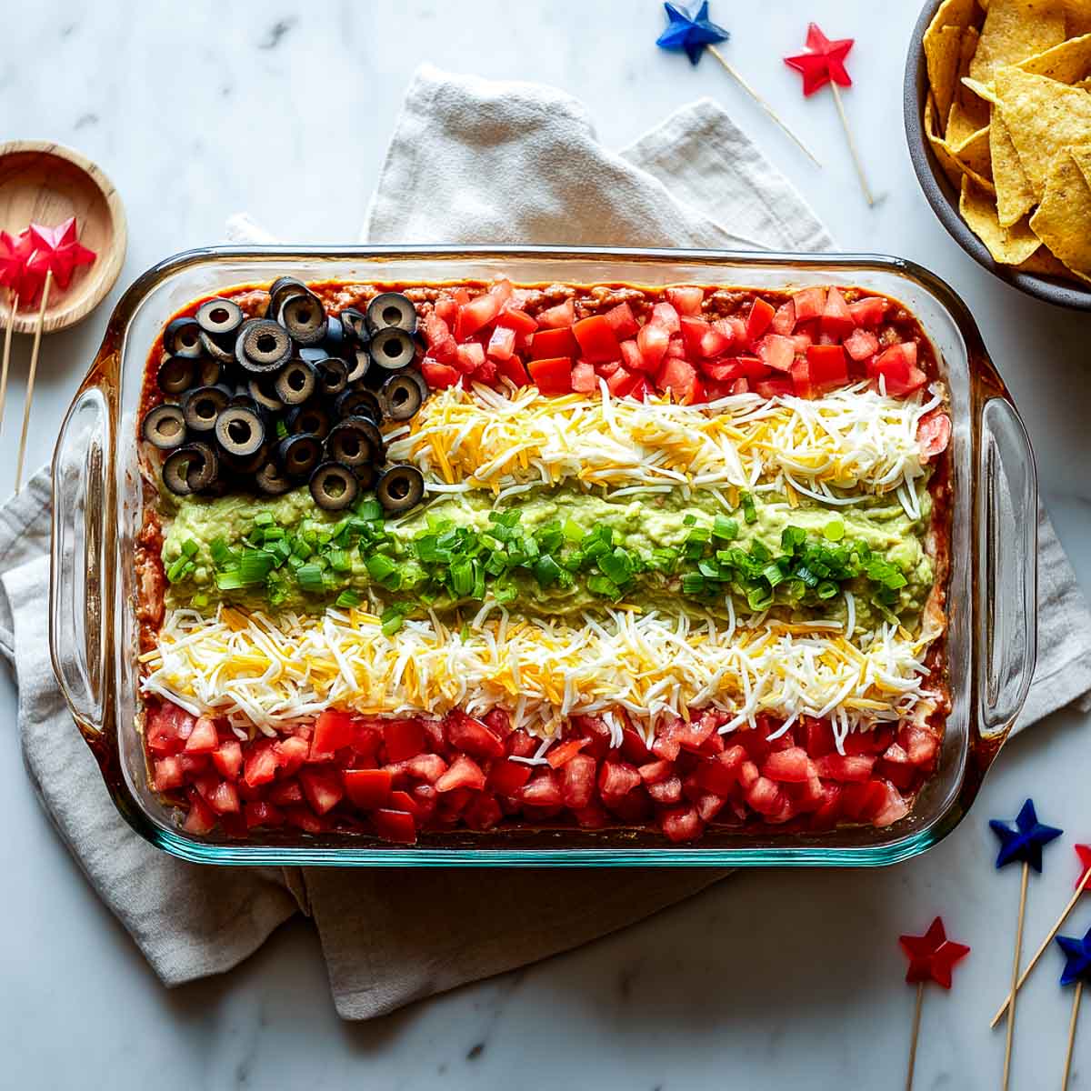 Layered taco dip styled as a flag with olives, tomatoes, and cheese.