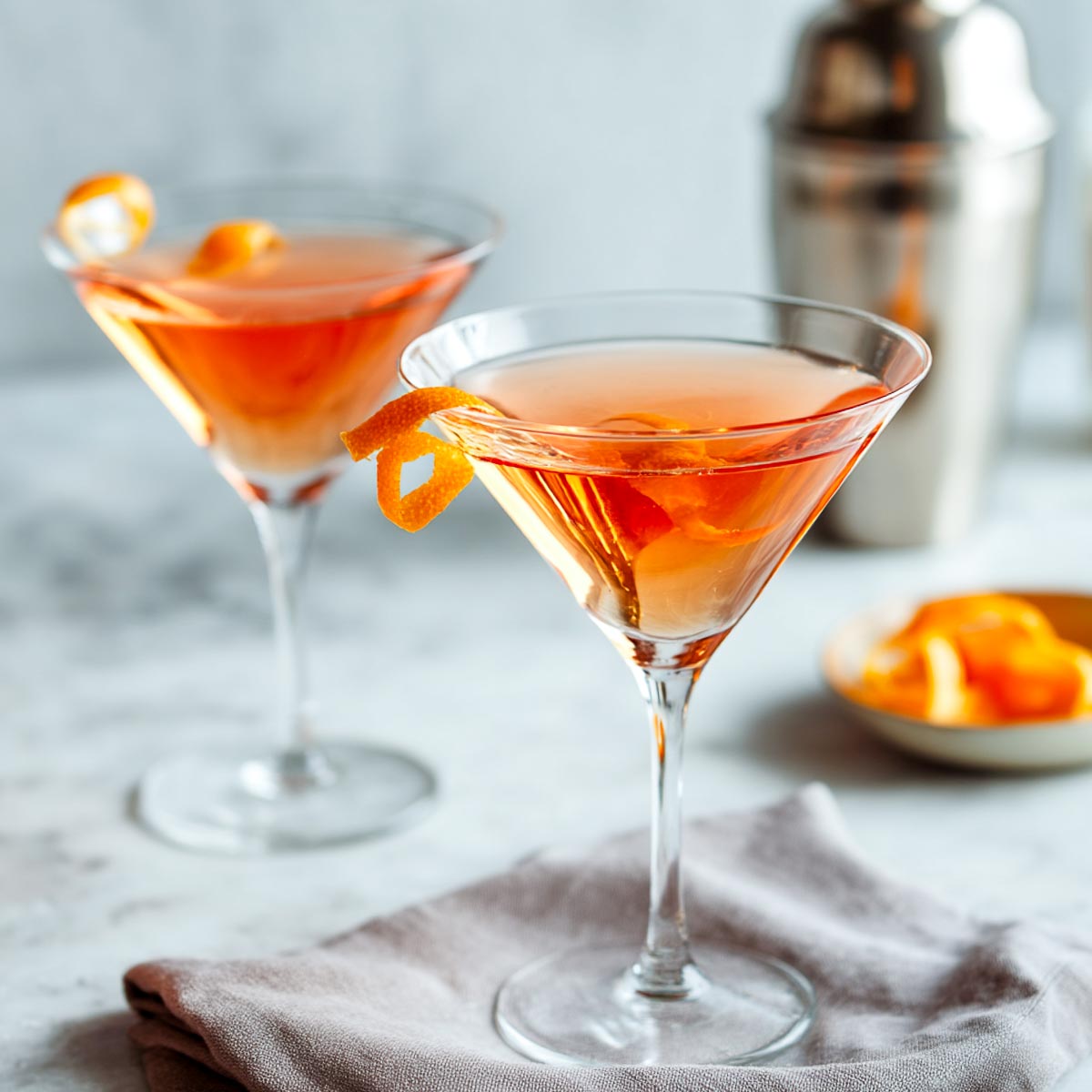 Two vodka martinis with Aperol and orange twist on marble.