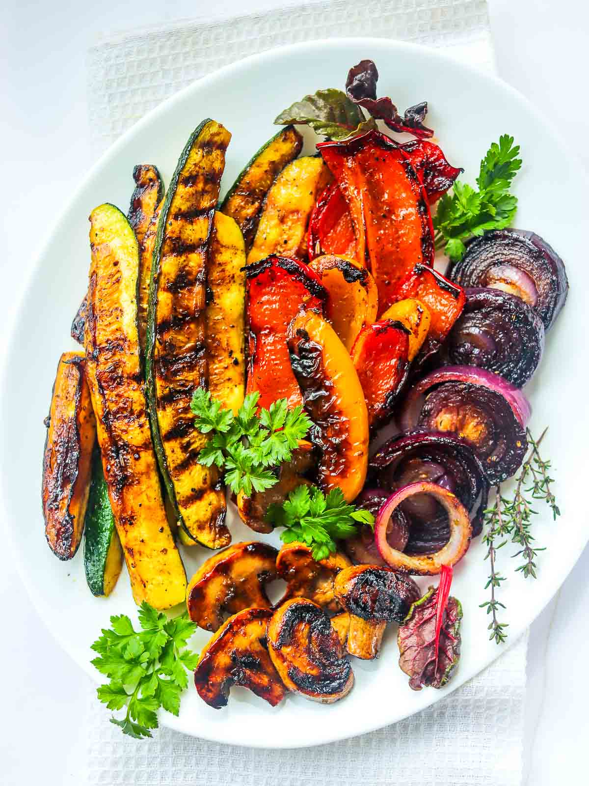 Grilled vegetables placed on a white oval plate and garnished with parsley.