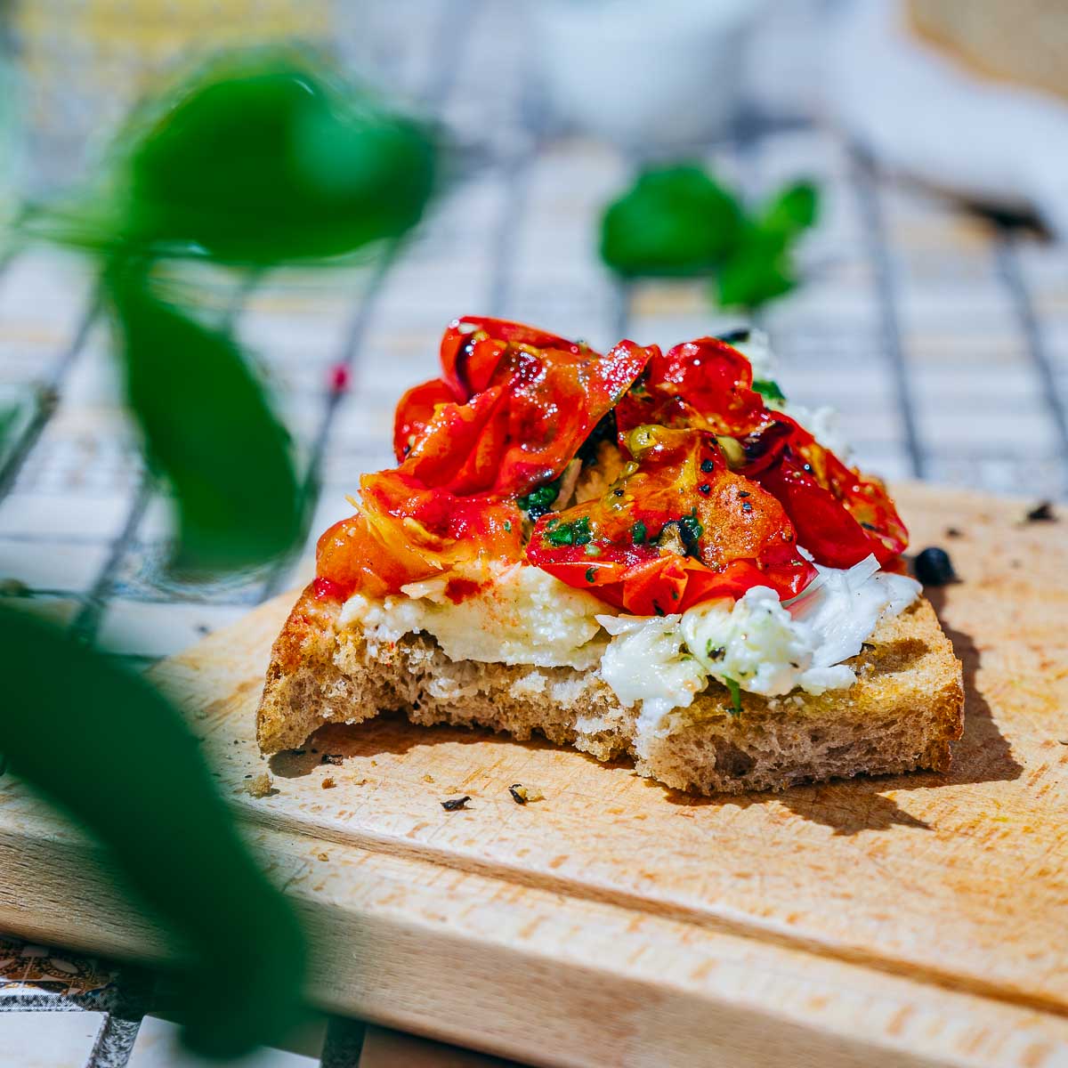 A bitten slice of burrata toast on a wooden board.
