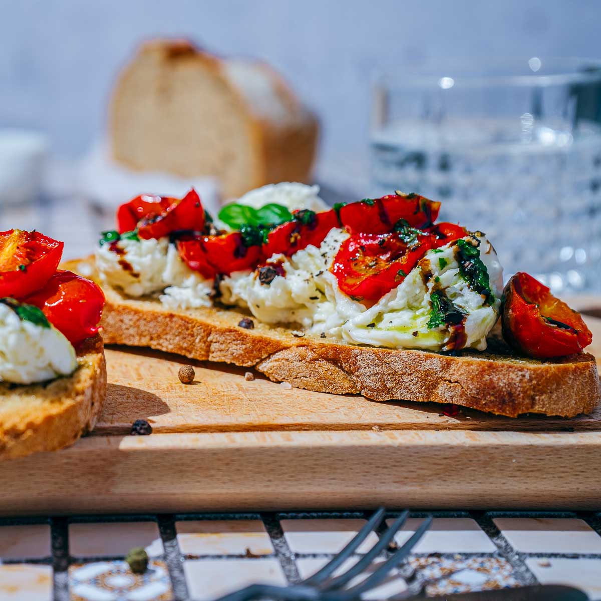 Side view of burrata toast with a loaf of sourdough bread in the background.