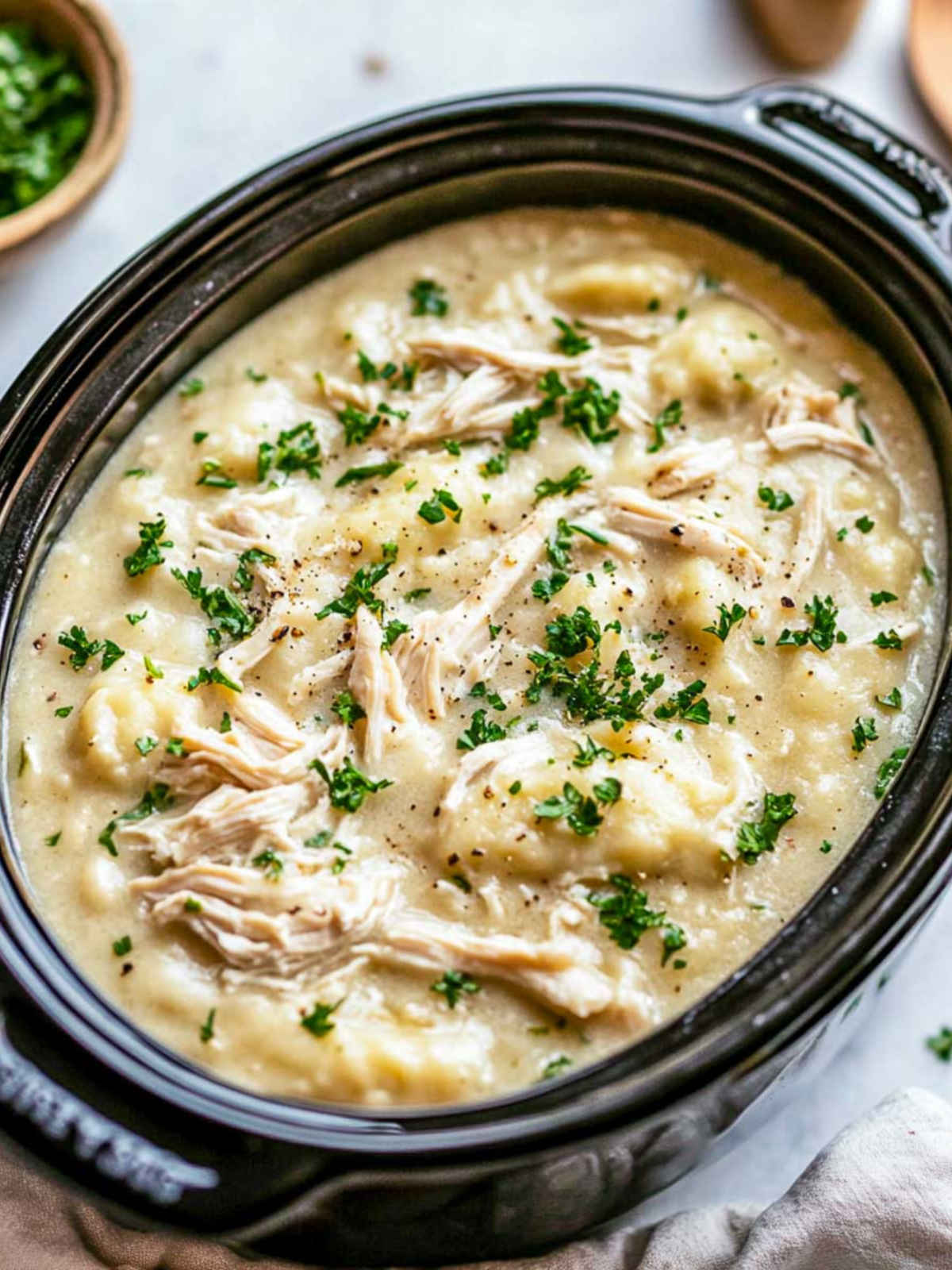 Chicken and dumpings in a crockpot placed on a white marble surface.