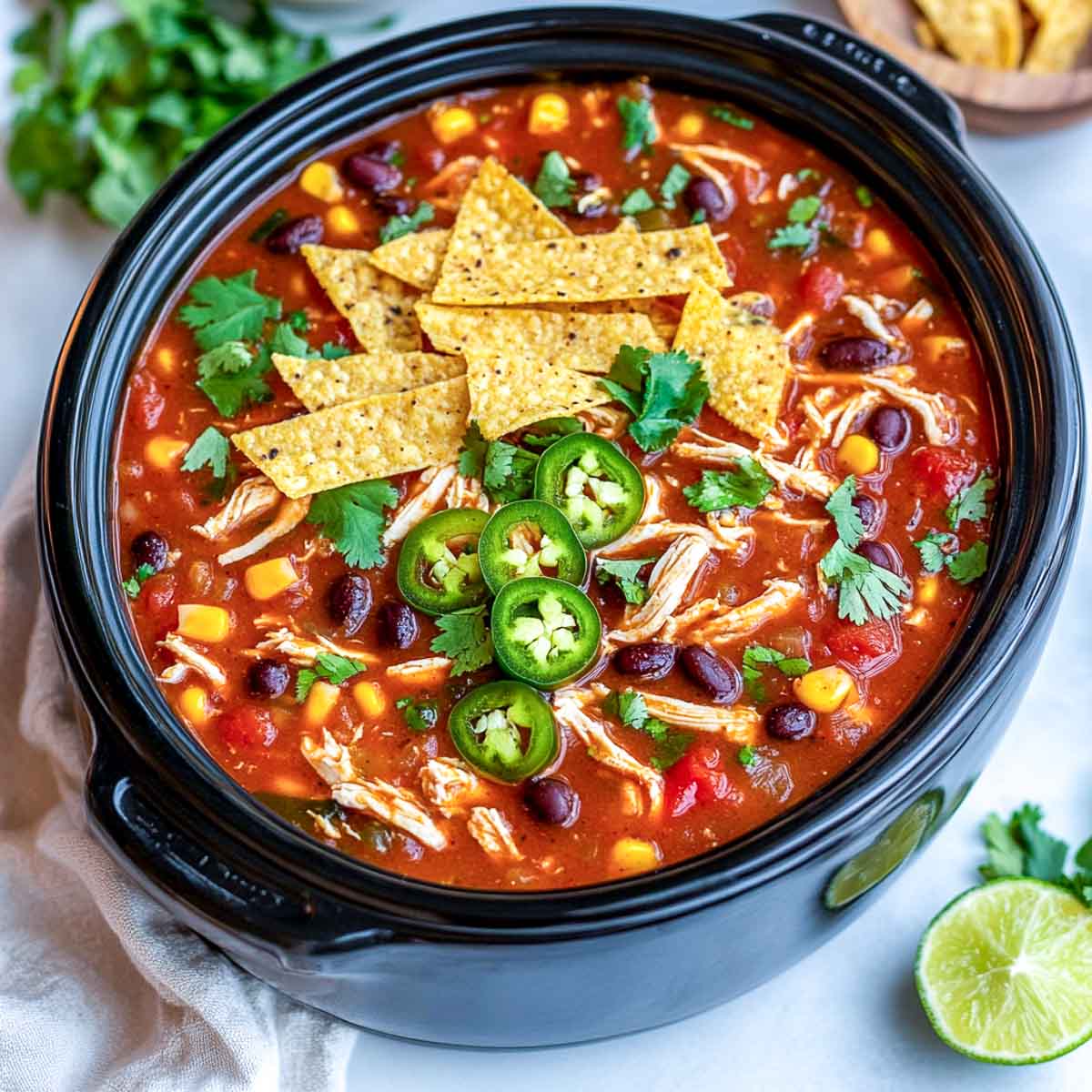 Crockpot chicken tortilla soup in a slow cooker, garnished with sliced jalapeños, tortilla strips, corn, beans, and fresh cilantro.