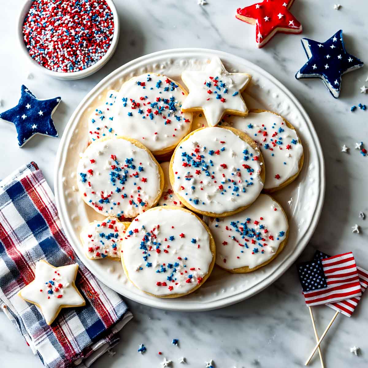 Top-down view of iced sugar cookies with red and blue sprinkles on marble.