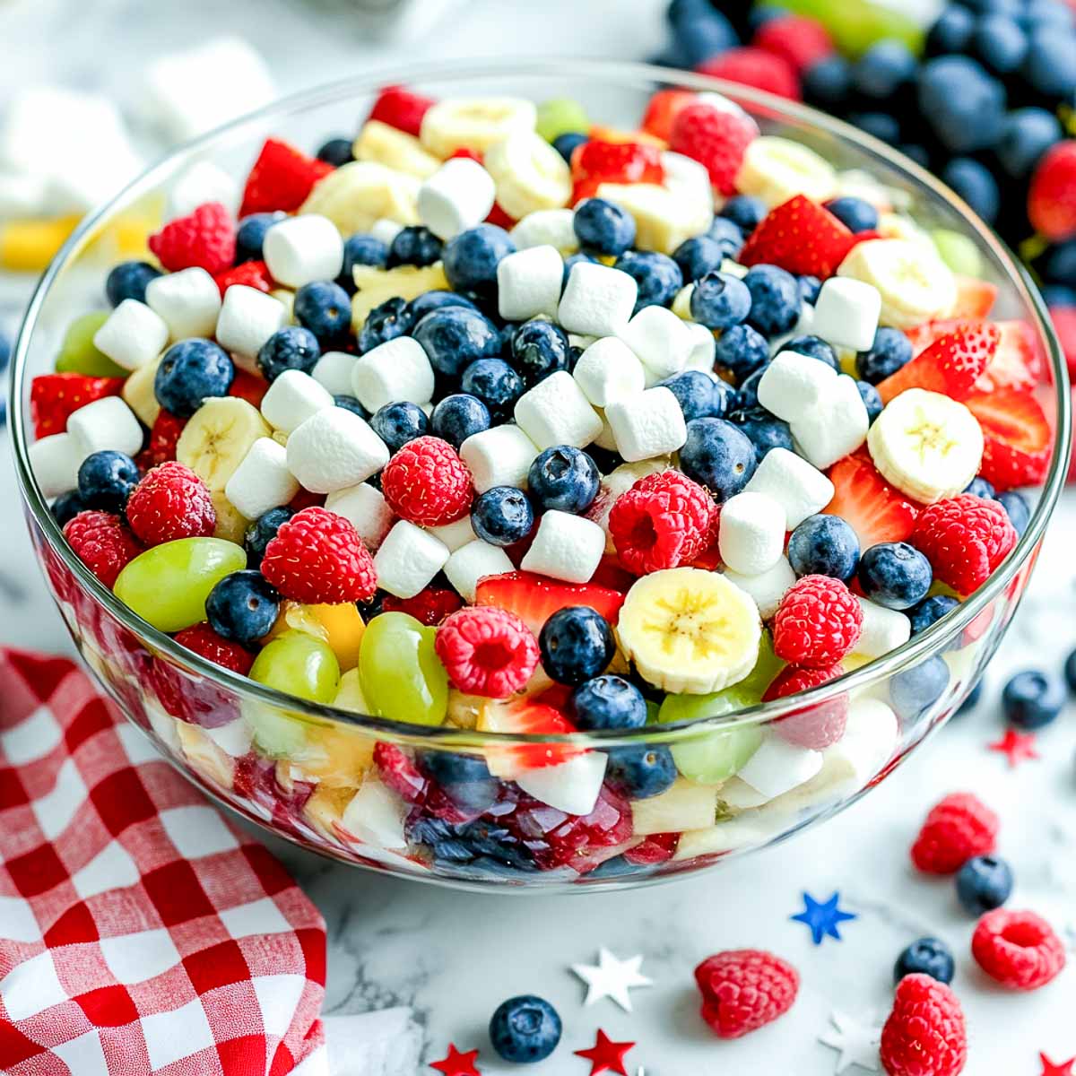 Fresh fruit salad with marshmallows, berries, banana, and grapes in a glass bowl.