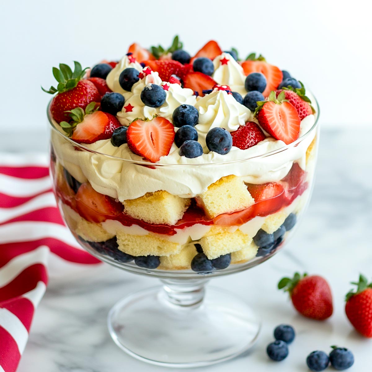 Layered fruit trifle with cake cubes, whipped cream, strawberries, and blueberries.