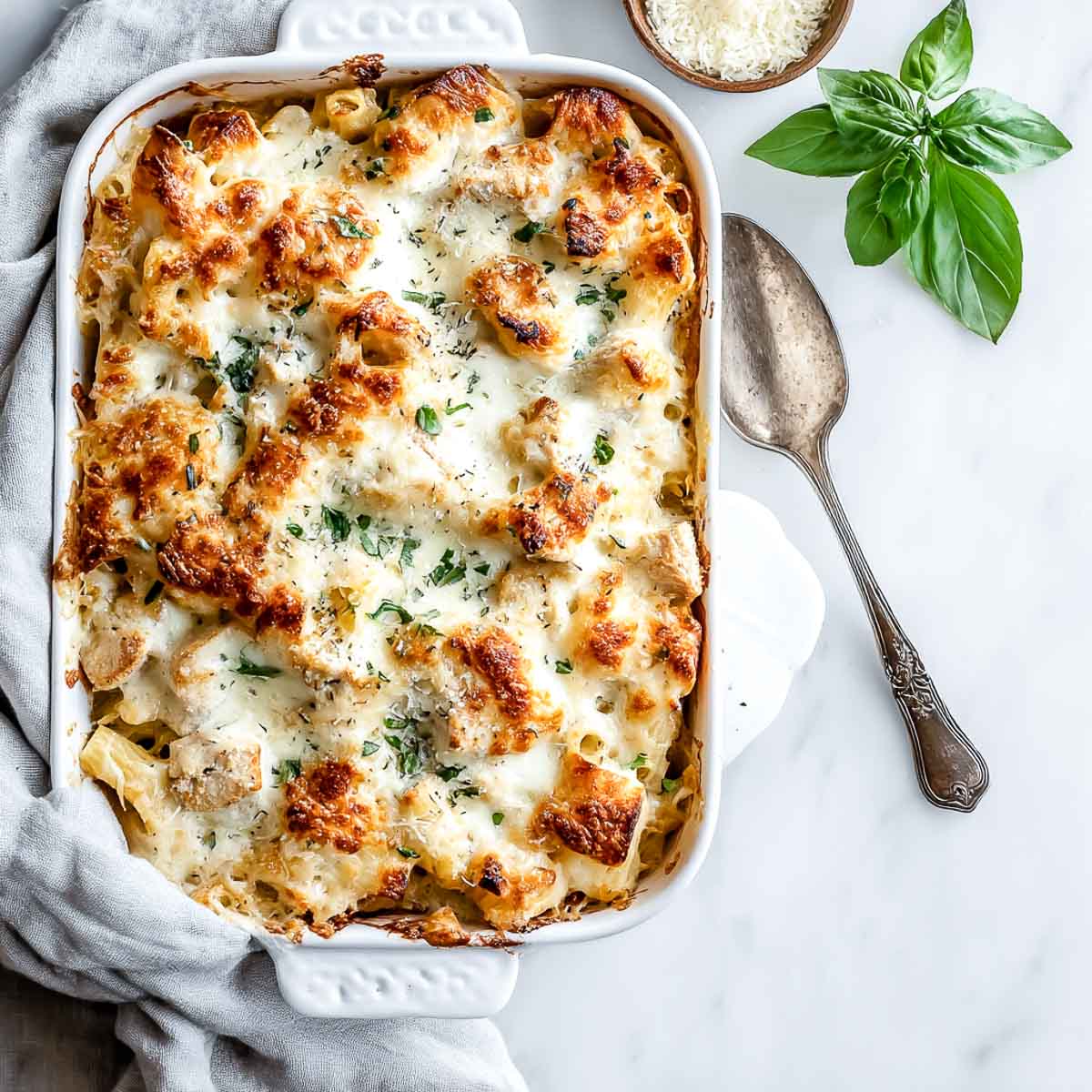 Golden-baked chicken Alfredo casserole with bubbly cheese in white dish.