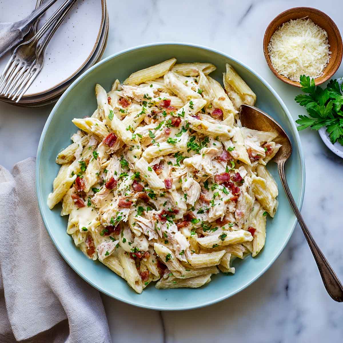 Creamy chicken pasta with bacon and parsley served in a green bowl.