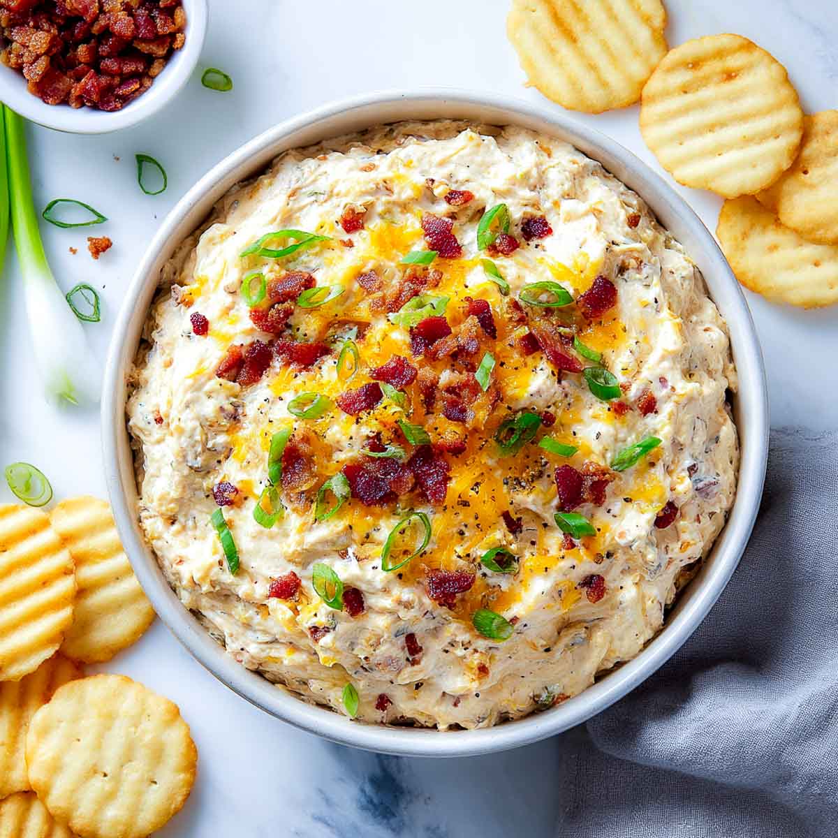 Creamy dip topped with bacon, cheese, and green onions in a white bowl.