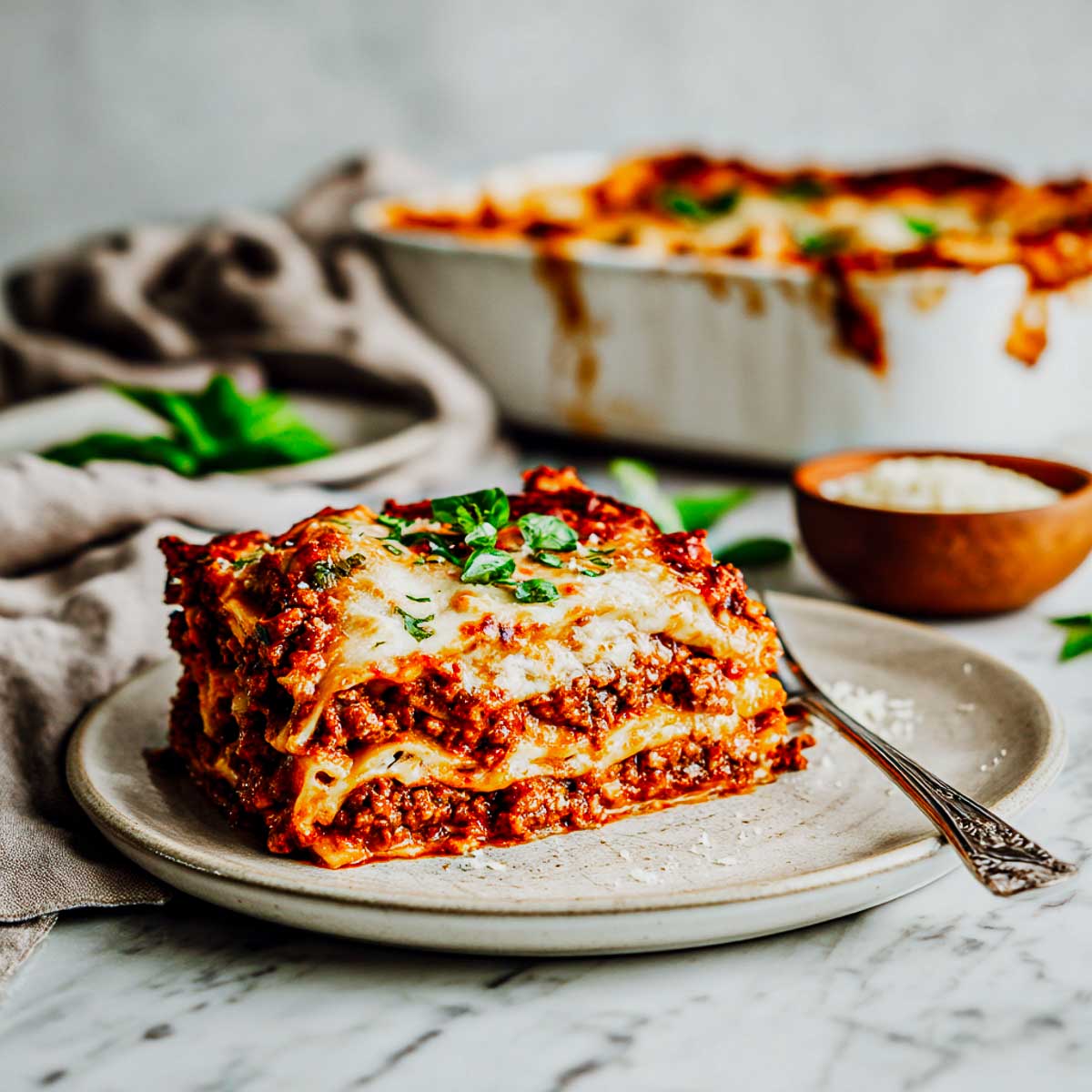 Layered lasagna slice with meat sauce and cheese on a white plate.