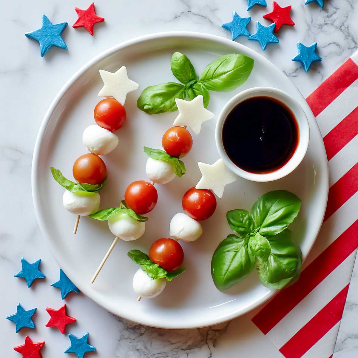 Mini caprese skewers with star mozzarella, basil, and tomatoes on white plate.