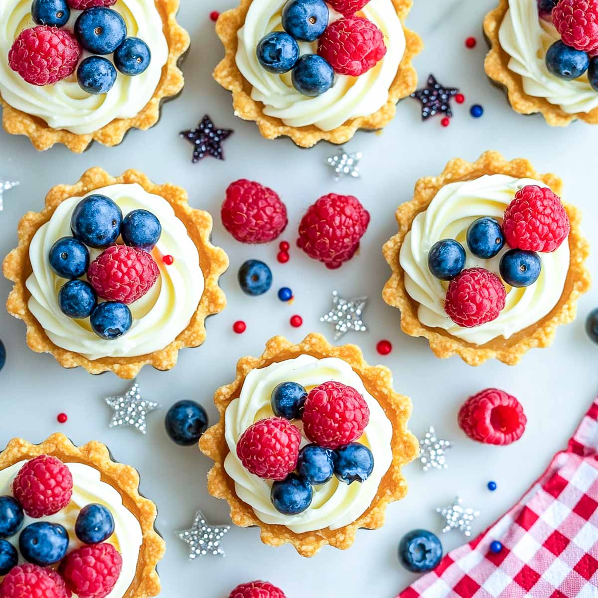 Mini no-bake fruit tartlets with cream filling, raspberries, blueberries, and festive sprinkles.