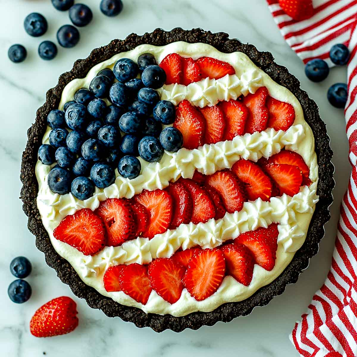 Oreo cookie crust pie decorated with strawberries, blueberries, and piped whipped cream stars.
