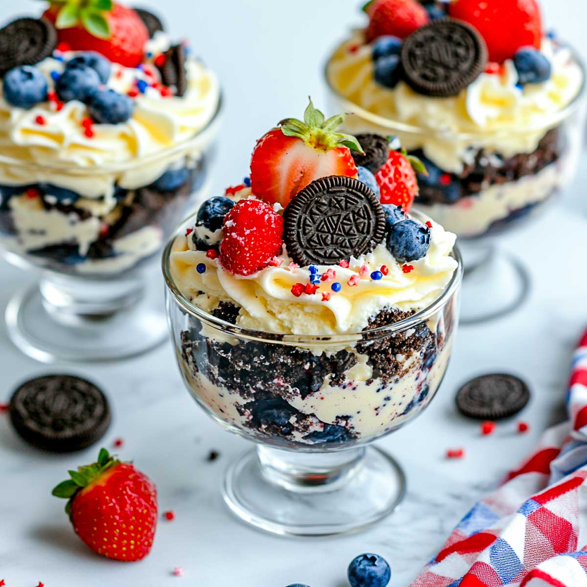 Oreo trifles with layers of cream, crushed Oreos, blueberries, and strawberries topped with whipped cream.