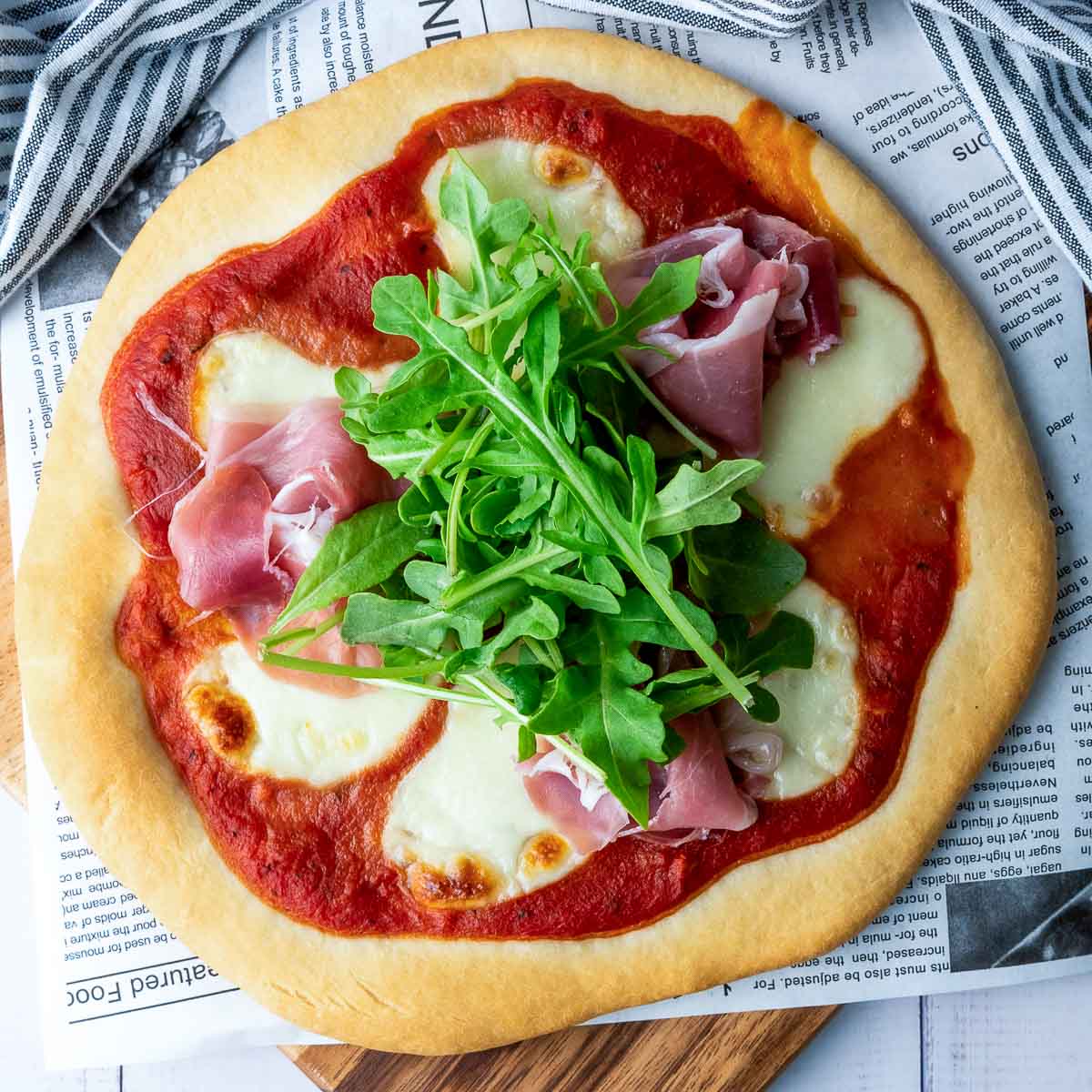 Top-down view of baked pizza topped with tomato sauce, mozzarella, prosciutto, and arugula.