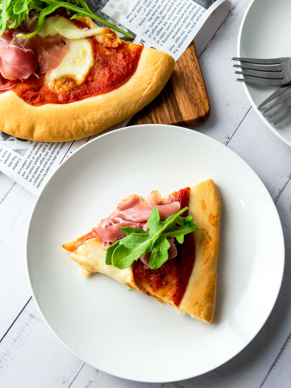 Slice of homemade pizza served on a white plate with melted mozzarella and arugula.