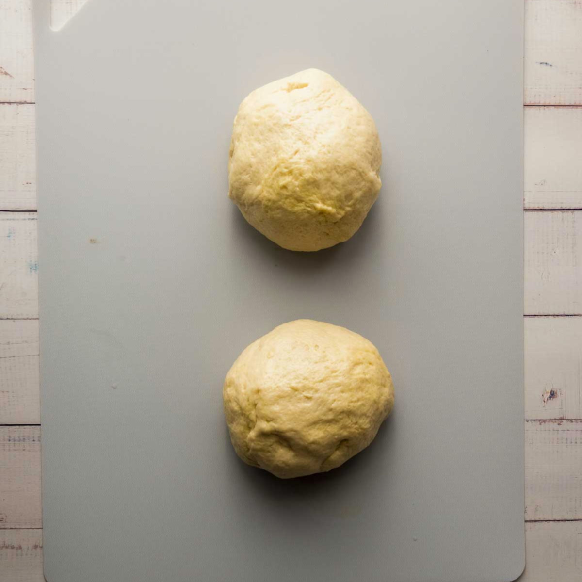 Dough divided into two equal balls on a cutting board.
