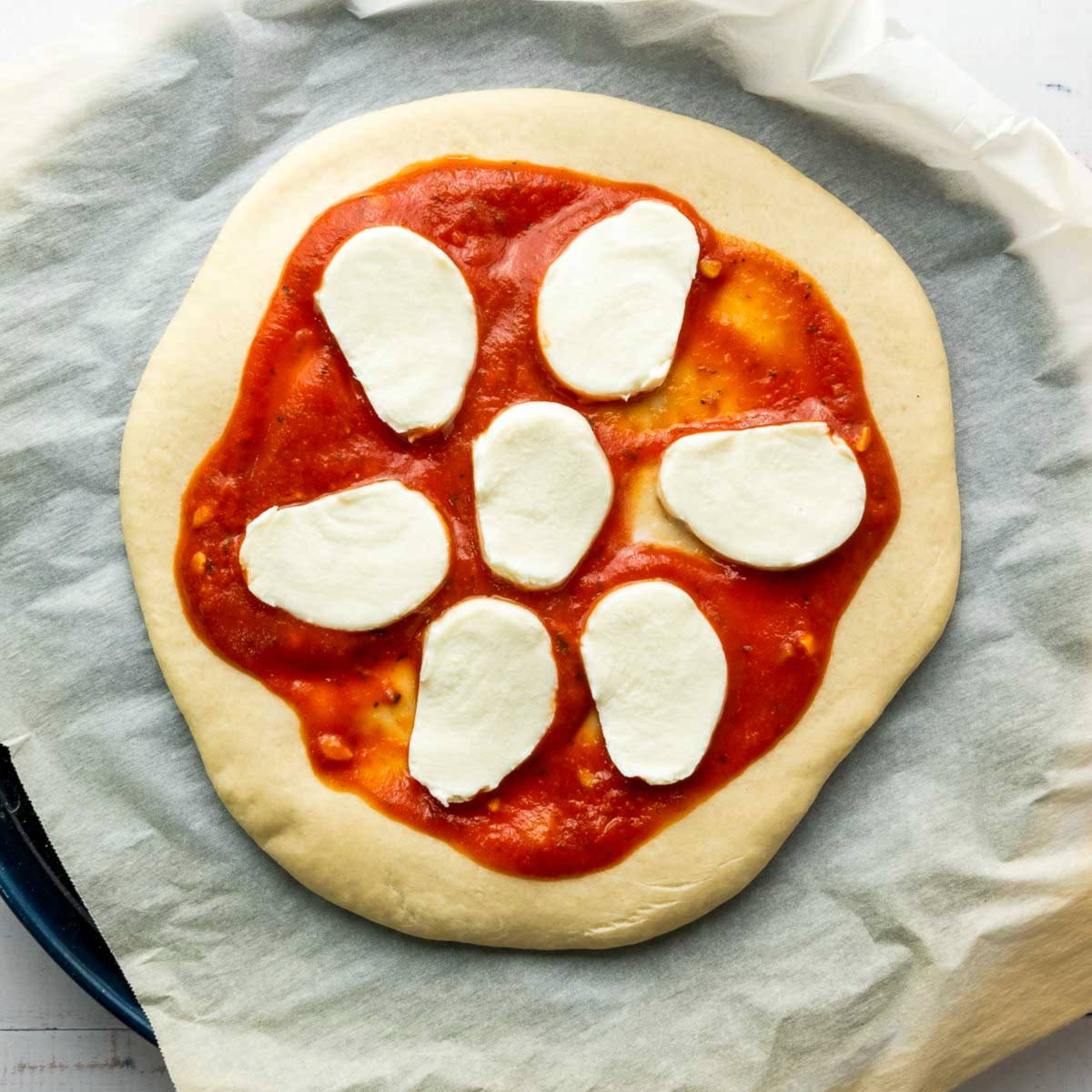 Parbaked pizza crust topped with tomato sauce and mozzarella slices.