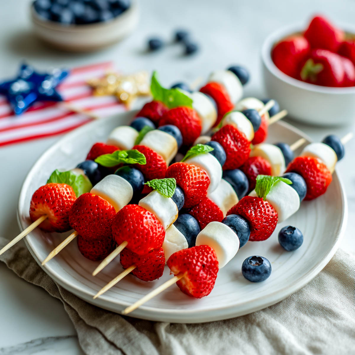 Fruit kabobs with strawberries, marshmallows, and blueberries on a white plate.