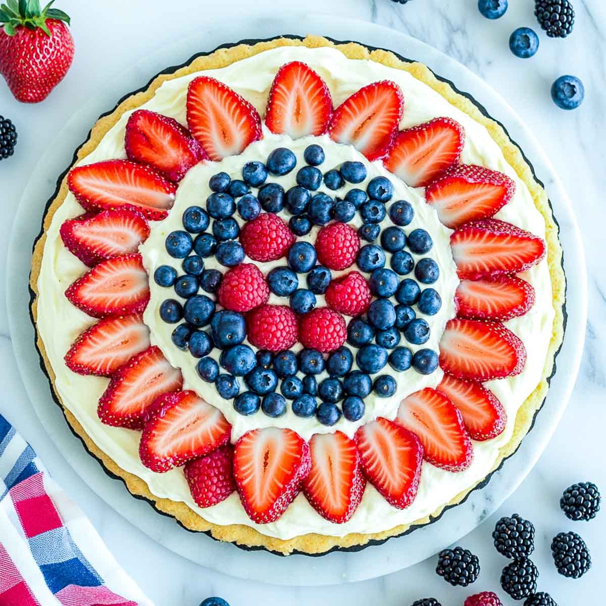 Patriotic fruit pizza topped with strawberries, blueberries, raspberries, and blackberries on a sugar cookie crust.