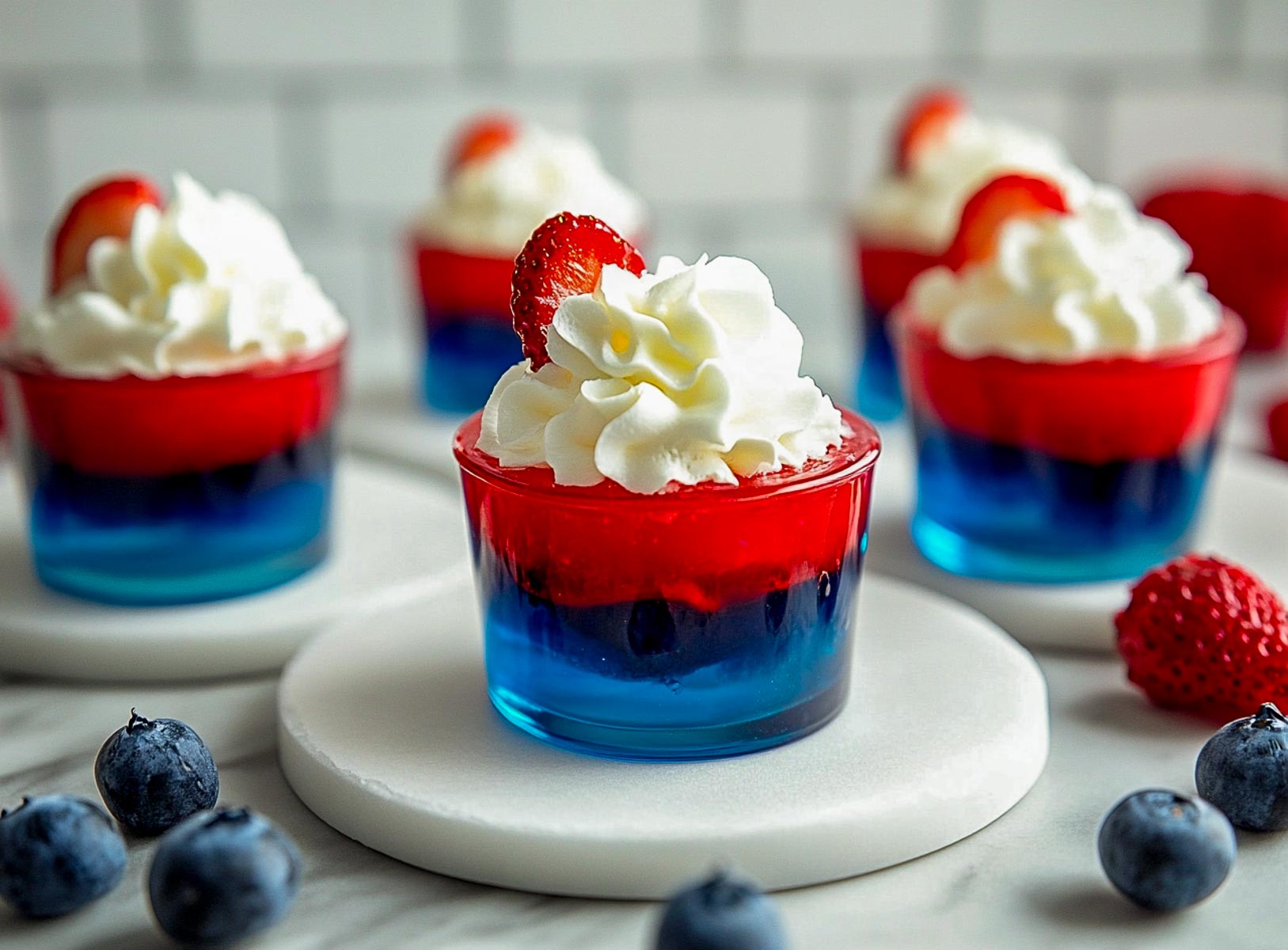 Red, white, and blue Jello cups topped with whipped cream and fresh berries.
