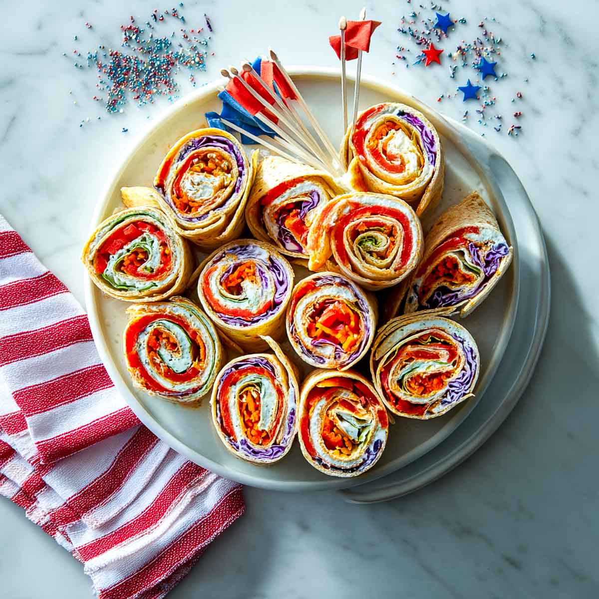 Tortilla pinwheels with red bell pepper, cream cheese, and cabbage on a round plate.